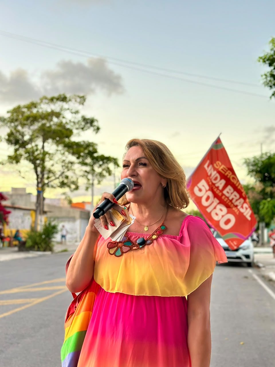 Linda Brasil fala ao microfone ao lado da bandeira 50180 durante caminhada em bairro de Aracaju